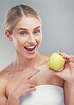 Happy woman pointing to green apple on studio background for healthy skincare, vegan diet and lifestyle nutrition. Portrait of smile female model holding fruit for wellness, detox snack and vitamins 