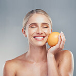 Woman, smile and orange fruit for skincare, beauty and health against grey studio background for cosmetics. Model. skin and face health for self care, vitamin c and cosmetic for organic dermatology