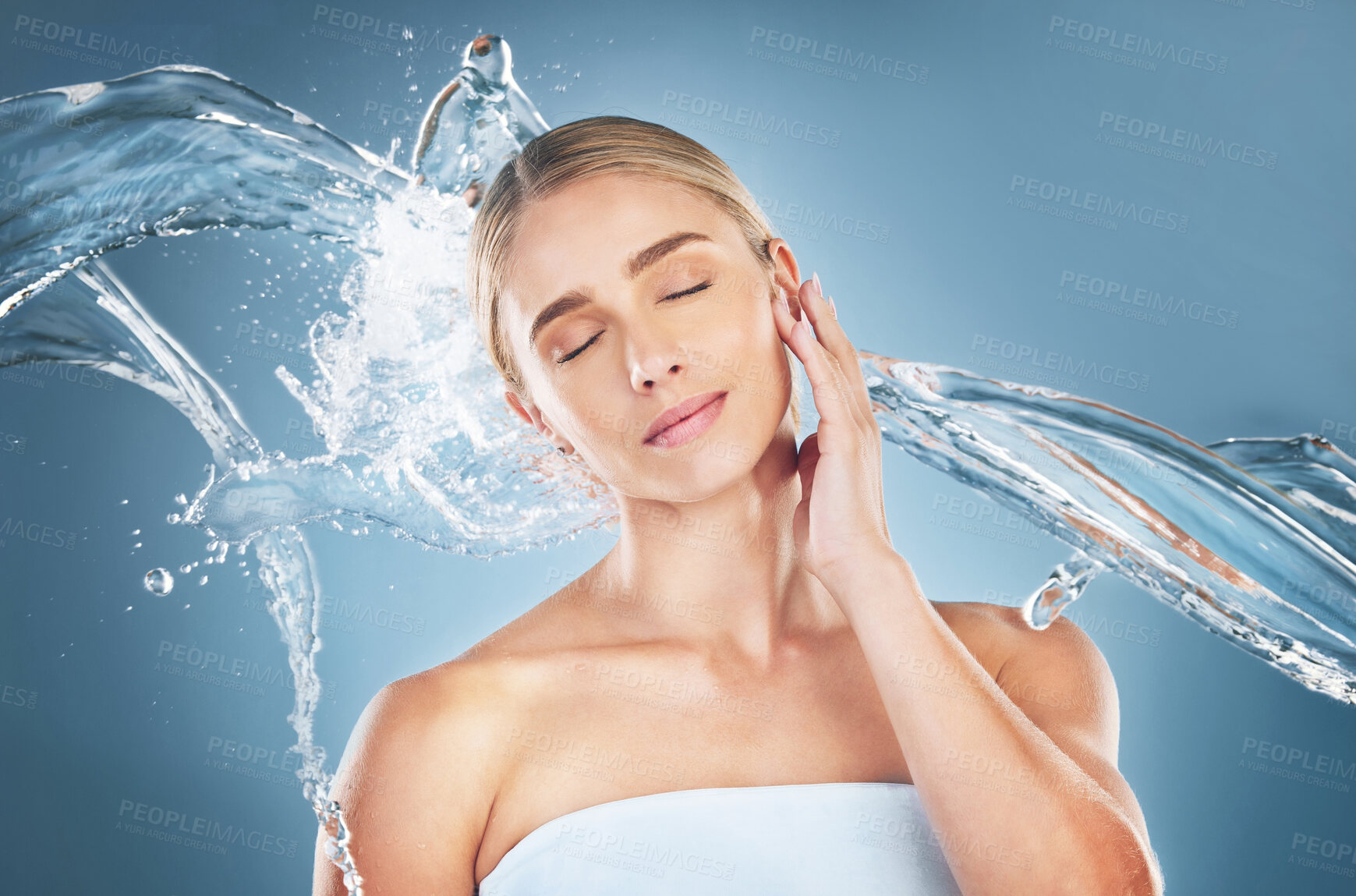 Buy stock photo Face, beauty and water splash of woman with eyes closed isolated on a blue background in studio. Skincare hygiene, facial cleaning and young female model from Canada feeling refreshed and healthy.