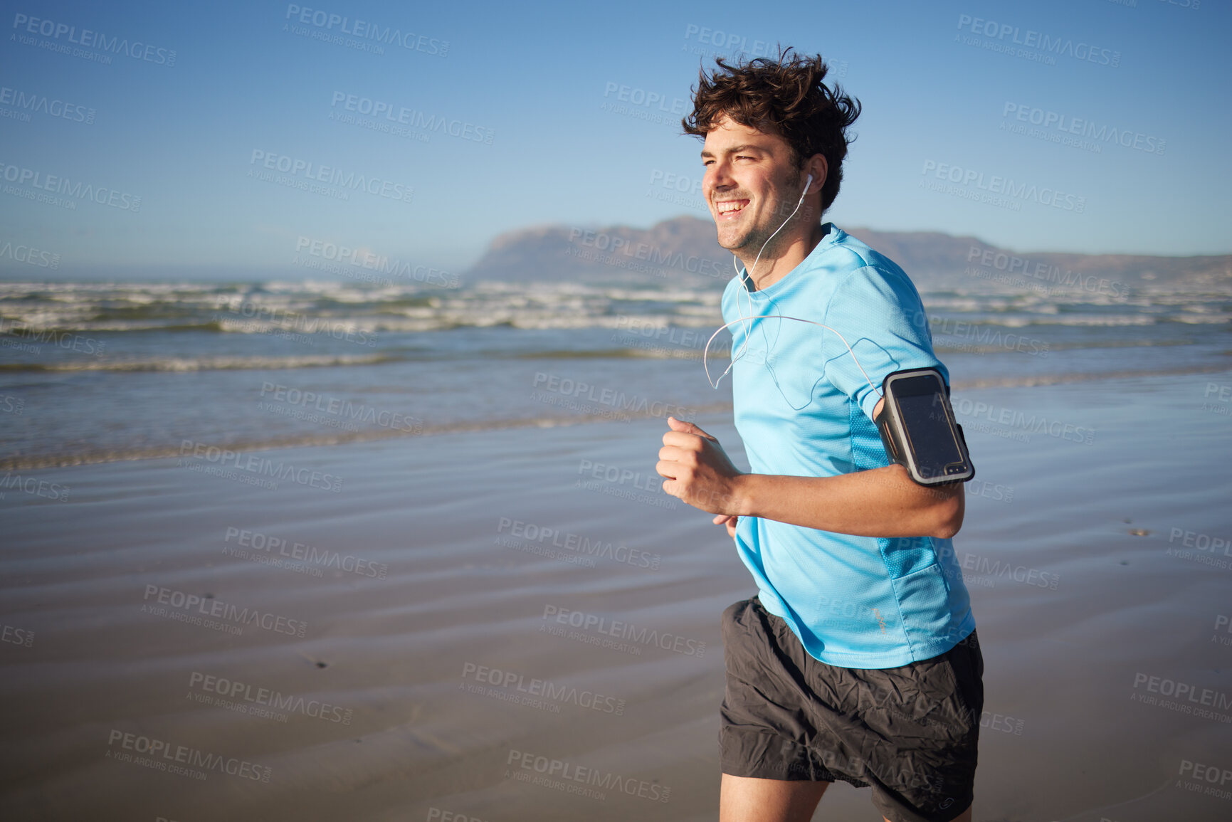 Buy stock photo Music, fitness and man running on beach, happy and relax with radio, audio and morning cardio. Podcast, exercise and guy runner training along the ocean, smile and enjoy summer, wellness and workout