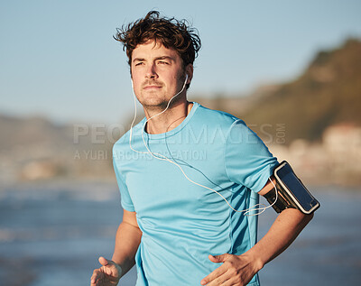 Buy stock photo Running, music and man athlete at beach with headphones run by the ocean with audio streaming. Mobile radio, web podcast or training song of a runner athlete listening to a track on an outdoor run