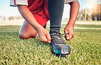 Sports, football field and child tie shoes for match workout, challenge contest or practice exercise on grass pitch. Athlete fitness health, training black kid or youth soccer player ready for game 
