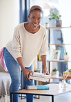 Cleaning, housework and books with a black woman cleaner packing in a home living room. Apartment, housekeeping and chores with a young female in a house to clean or tidy while working as a maid