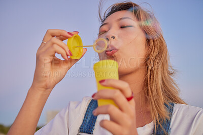 Buy stock photo Asian, soap and bubbles of woman youth enjoying vacation, freedom and wellness on peaceful evening. Calm, relax and peace of girl in Japan blowing bubbles with tranquil sunset sky in summer.
