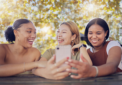 Buy stock photo Phone, friends and social media with a woman group typing a text message while sitting in a park together during summer. Internet, app and mobile with a female and friend laughing at a meme online