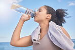 Water, fitness and woman with a drink after exercise, workout or training by the sea. Sports, motivation and energy from a runner with a bottle for hydration after running by the beach in nature