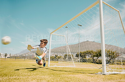 Soccer, sports and children with a goalkeeper saving a shot during a competitive game on a grass pitch or field. Football, kids and goal with a male child diving to save or stop a ball from scoring