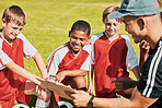 Soccer, children and coach with clipboard talking game plan, team training and formation on soccer field outdoor for fitness, competition and sport. Man talking to junior football group planning game