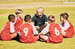 kids, soccer and team coach planning training with clipboard on soccer field for sport competitiion together. Athlete children, teamwork and sit on grass before football match or workout outdoors