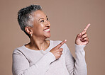 Mature woman pointing to space on studio background for marketing, advertising or presentation of ideas, choice and review. Happy lady showing brown mockup, offer and branding of commercial promotion