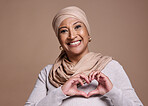 Hands, heart and muslim with a mature woman in studio on a brown background to promote love or health. Portrait, hand sign and Islam with a senior female posing for healthcare, affection or culture