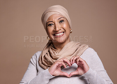 Buy stock photo Hands, heart and muslim with a mature woman in studio on a brown background to promote love or health. Portrait, hand sign and Islam with a senior female posing for healthcare, affection or culture