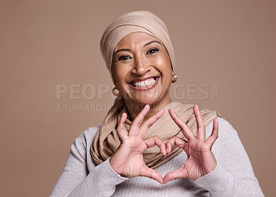 Buy stock photo Islam woman, heart and sign with smile, happy and peace against brown studio background. Muslim lady, mature female and hand gesture for happiness, love and commitment for humanity and positive.
