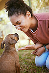 Happy black woman, pet puppy and play in garden, backyard or park for training, learning and behaviour. Woman, young dog and sitting on grass together for game, fun and happiness outdoor in nature