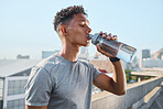 Fitness, exercise and man drinking water in city after running, training or cardio workout. Health, wellness and hydration of sports male from India resting or on break after marathon or sprinting.