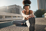 Stretching, foot and city black woman on floor with headphones, sneakers and training gear for outdoor running, exercise and workout. Sports, fitness and girl listening to music for muscle warmup