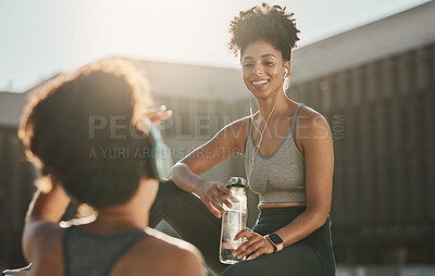 Buy stock photo Fitness, headphones and black women or friends in city on break with water bottle and talking. Health, wellness and people resting while streaming music, radio or podcast after running or training.