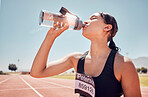 Fitness, water and runner woman training at running track, thirsty and relax after workout against a blue sky background. Sports, girl and drinking water at stadium after running, exercise and sport