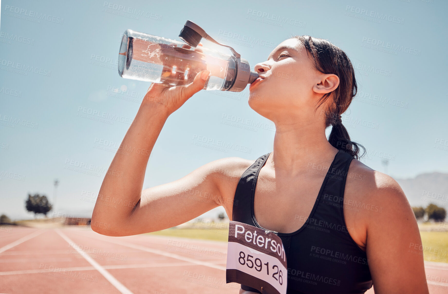 Buy stock photo Fitness, water and runner woman training at running track, thirsty and relax after workout against a blue sky background. Sports, girl and drinking water at stadium after running, exercise and sport