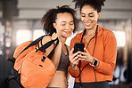 Gym, friends and women looking at phone, fitness app and planning workout schedule or checking training progress. Exercise, friendship and smartphone, woman and personal trainer checking social media