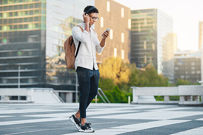 Buy stock photo Phone, music and city with a man student walking to university or college during his morning commute. Headphones, social media and 5g mobile technology with a male pupil in an urban town for a walk