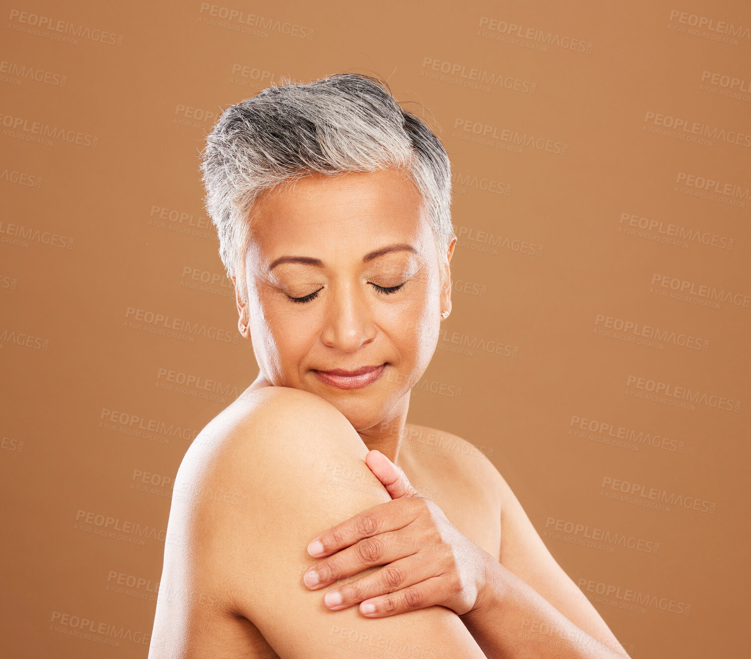 Buy stock photo Face, skincare and senior woman with eyes closed in studio on a brown background. Aesthetics, makeup and cosmetics of mature female model from India touching skin or arm for healthy skincare routine.
