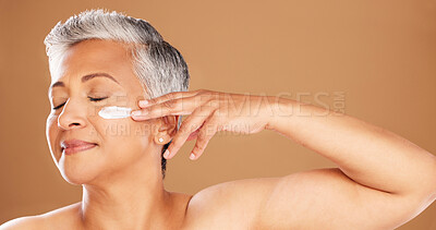 Buy stock photo Cream, skincare and senior woman with peace, wellness and care for skin against a brown studio background. Smile, dermatology and calm elderly model with sunscreen for facial and body health