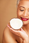 Beauty, skincare and coconut with a senior woman in studio on a brown background to promote natural antiaging care. Cosmetics, moisture and hydration with a mature female posing with a fruit half