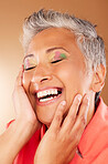 Happy, color and senior woman with makeup standing in a studio with colorful, trendy and edgy cosmetics. Happiness, smile and elderly lady with a beauty routine isolated by gradient brown background.