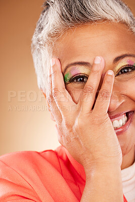 Buy stock photo Makeup, comic and senior woman creative with color for face against a brown studio background. Playful, happy and hand of an elderly model with facial cosmetics for creativity, beauty and fashion