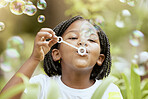 Bubbles, playful and African girl in nature with freedom, smile and playing in a park. Spring, happy and carefree child with a bubble game in a backyard or field with plants for happiness and youth