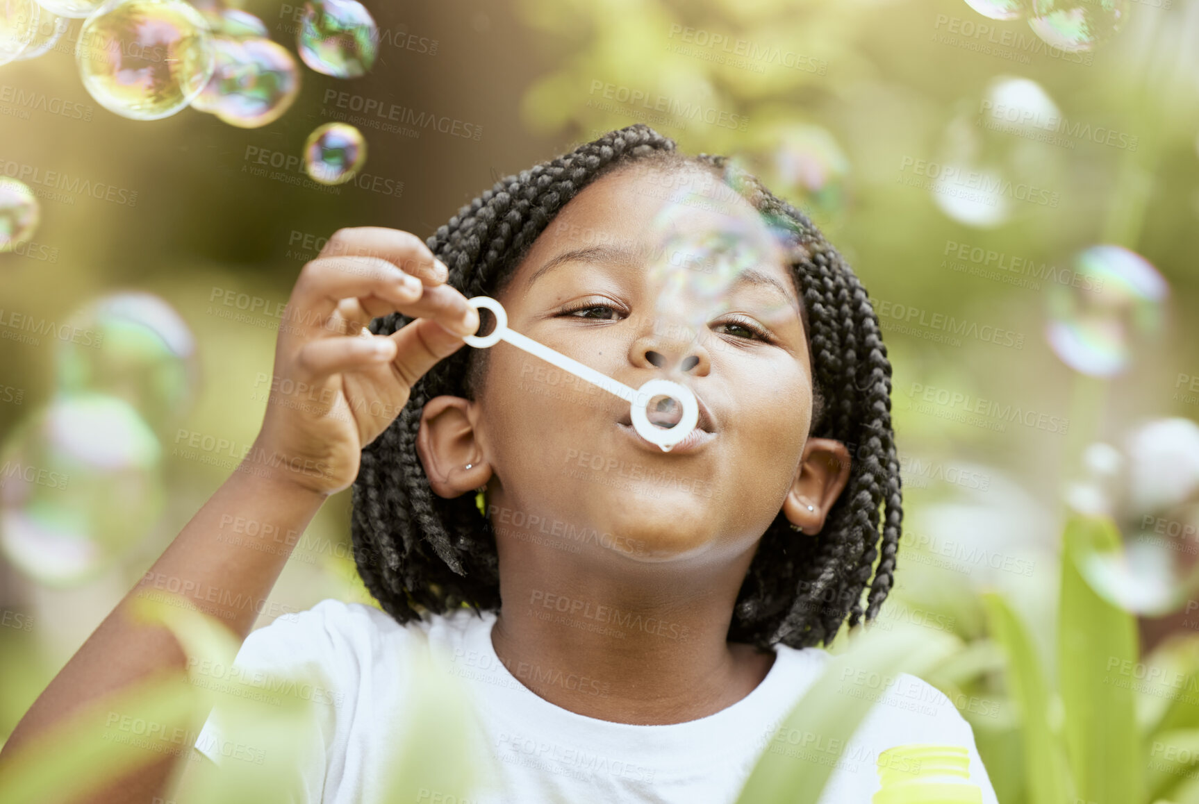 Buy stock photo Bubbles, playful and African girl in nature with freedom, smile and playing in a park. Spring, happy and carefree child with a bubble game in a backyard or field with plants for happiness and youth