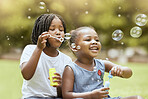 Black kids, children and blowing bubbles at park, having fun and bonding. Girls, happy sisters and playing with soap bubble toys, relax and enjoying quality time together outdoors in nature on grass
