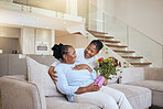 Mothers day, black woman and surprise flowers on sofa for present, box or gift to mom in living room. Woman, bouquet or senior mama on couch with wow, happy or smile for love, celebration or birthday