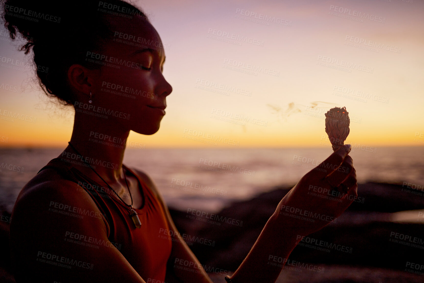 Buy stock photo Sunset meditation, woman relax in by beach and ocean for zen peace focus, chakra wellness and mental health by the sea. Burning sage in nature, aromatherapy and spiritual mindfulness health exercise 