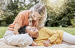 Happy family, interracial and girl and mother relax in a park, happy and smile while resting on grass together. Love, family and black child laughing with her mom, cheerful and peaceful in a yard