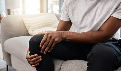 Buy stock photo Knee pain, hand of a man and injury while sitting on home living room sofa for rest and relaxation. Ache, painful leg joint and african american man touching his knees for a strain muscle 