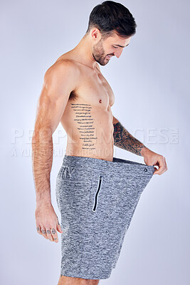 Buy stock photo Motivation, diet and weight loss, man checking pants size change from workout and healthy lifestyle on studio background. Fitness, nutrition and wellness, balance in body care, male model with tattoo