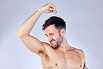 Armpit, stink and hygiene with a man model smelling his underarm in studio on a gray background for a deodorant product. Body, natural and sweat with a handsome young male sniffing his sweaty arm