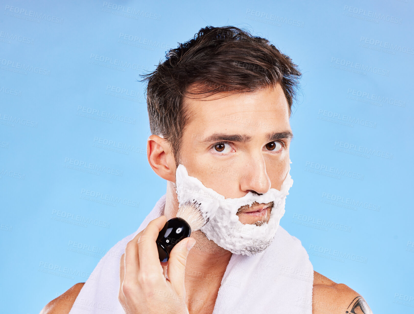 Buy stock photo Face, shave and grooming with a man model shaving his skin for hair removal in studio on blue background. Portrait, brush and hygiene with a handsome young male in the bathroom for a morning routine