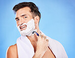 Face, shave and hair removal with a man model shaving his skin in studio on a blue background for wellness or hygiene. Portrait, beard and razor with a young male grooming alone in the bathroom