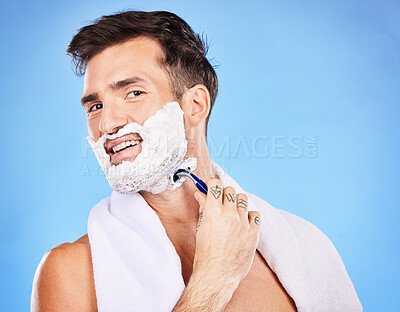 Buy stock photo Face, shave and hair removal with a man model shaving his skin in studio on a blue background for wellness or hygiene. Portrait, beard and razor with a young male grooming alone in the bathroom