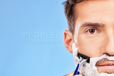 Buy stock photo Face, shave and grooming with a man model shaving his beard in studio on a blue background with mockup. Portrait, closeup and razor with a handsome young male in the bathroom for hair removal