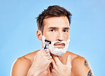 Portrait, shave and razor with a man model grooming in studio on a blue background for wellness or care. Face, skin and shaving with a handsome young male in the bathroom for facial hair removal