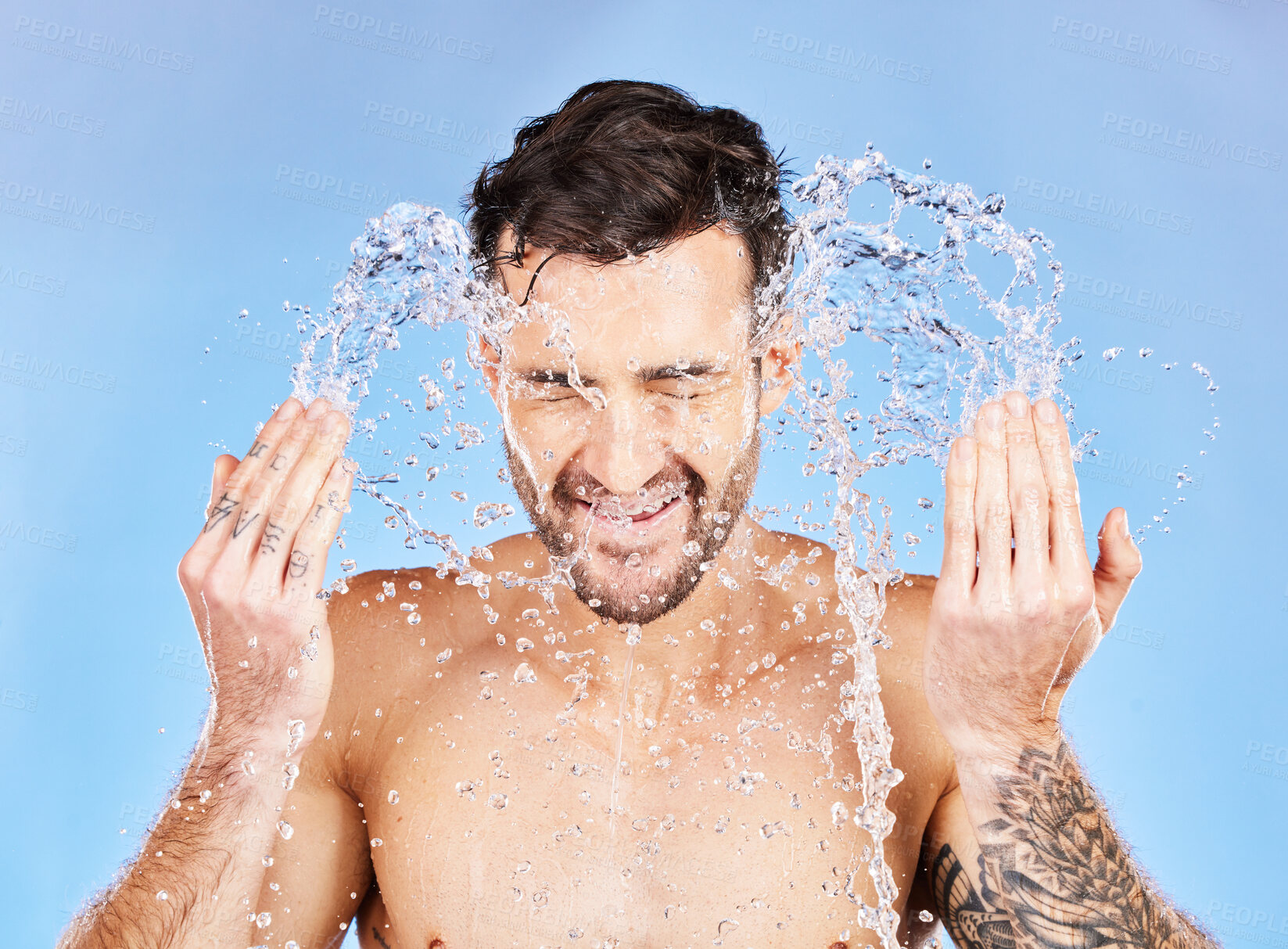 Buy stock photo Face, water and cleaning with a man model splash in studio on a blue background for hygiene. Skincare, water splash and hydrate with a handsome young male washing his skin in the bathroom for care