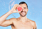 Shower, water and grapefruit with a man model in studio on a blue background for hygiene or hydration. Portrait, water splash and skincare with a handsome young male posing for natural body care