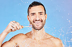 Shower, brushing teeth and hygiene with a man model in studio on a blue background with splash for oral care. Water, cleaning and dental with a handsome young male wet in the bathroom for wellness