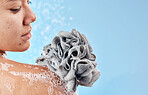 Shower, cleaning and loofah with a woman in studio on a blue background for water hydration or hygiene. Skincare, wellness and beauty with a female washing in the bathroom for luxury body care