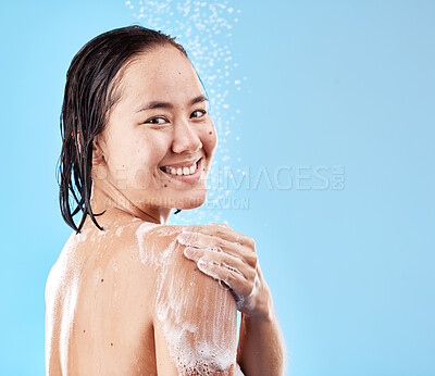 Buy stock photo Shower, woman and hygiene for wellness, smile and happy with cleaning, water and soap against blue studio background. Portrait, young female and lady doing scrub, washing and health with happiness.