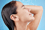 Shower, water drops and happy woman with hair care, facial cleaning and cosmetics in studio profile zoom. Asian, Japanese girl or young model in bathroom with water splash on face on blue background